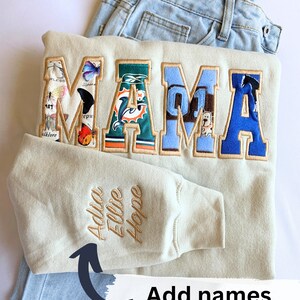 May include: A beige sweatshirt with the word "MAMA" spelled out in colorful fabric patches. The sweatshirt has a sleeve with the names "Addie, Ellie, Hope" embroidered on it.