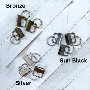 May include: An assortment of metal key fob hardware in bronze, gun black, and silver finishes. Each piece includes a rectangular clasp and a split ring. The word "Bronze", "Gun Black", and "Silver" are displayed in the image.