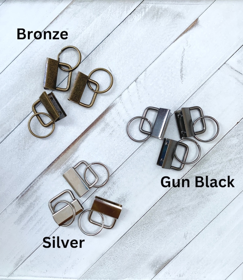 May include: An assortment of metal key fob hardware in bronze, gun black, and silver finishes. Each piece includes a rectangular clasp and a split ring. The word "Bronze", "Gun Black", and "Silver" are displayed in the image.