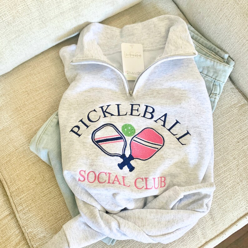 May include: Gray sweatshirt with a white and pink pickleball paddle design and the text "Pickleball Social Club".