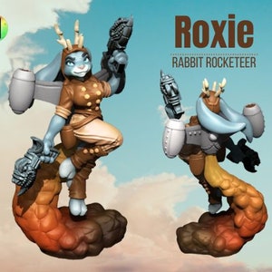 May include: A blue and brown rabbit figurine with wings and a rocket pack, standing on a brown and orange rock formation. The figurine is titled "Roxie Rabbit Rocketeer".