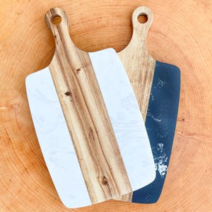 Op de afbeelding: Twee houten snijplanken met verschillende ontwerpen. Een plank heeft een wit marmerontwerp en de andere een zwart marmerontwerp.