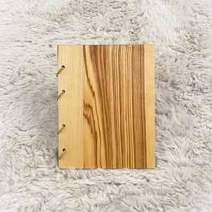 Może przedstawiać: Drewniany dziennik z naturalnym usłojeniem drewna i brązową skórzaną oprawą. Dziennik ma rustykalny wygląd i idealnie nadaje się do zapisywania myśli, pomysłów lub wspomnień.