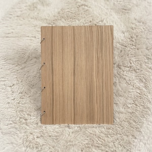 Op de afbeelding: Een houten dagboek met een natuurlijke houtnerf. Het dagboek heeft een gestikte binding en is gesloten.