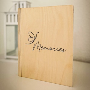 Può includere: Un album fotografico in legno con un design a farfalla e il testo "Our Memories" inciso sul davanti.