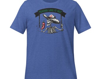 Puede incluir: Camiseta azul con un diseño de esqueleto con sombrero de vaquero y un chile rojo. El texto "Texans Like It Hot" está sobre el esqueleto en una pancarta.