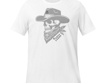 May include: White t-shirt featuring a gray skull wearing a cowboy hat and bandana. The bandana has the word "Texas" printed on it. The skull has a crossbones design on the hat.