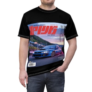 May include: Black t-shirt featuring a graphic of a blue car on a road, with Japanese text and the word "ppan WRX". The design resembles a magazine cover. The shirt has a crew neck and short sleeves.