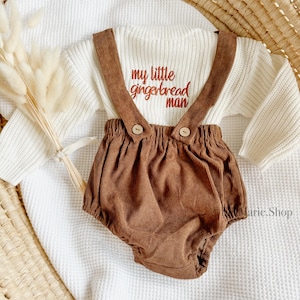 May include: A white knitted sweater with brown corduroy overalls. The sweater has the text "my little gingerbread man" embroidered on the front.