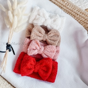 Könnte beinhalten: Vier flauschige Stirnbänder in verschiedenen Farben: Weiß, Braun, Rosa und Rot. Jedes Stirnband hat eine große Schleife in der Mitte.