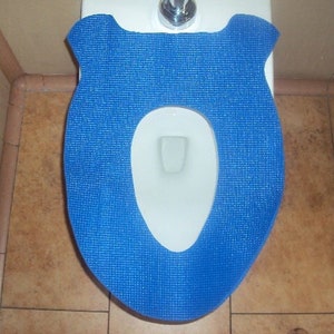 Puede incluir: Una tapa de asiento de inodoro azul con una superficie texturizada. La tapa está diseñada para adaptarse a un asiento de inodoro estándar.