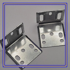May include: Two silver-colored, right-angle metal brackets. Each bracket has a flat base with multiple circular and oblong holes for screws. The brackets are designed to connect two surfaces at a 90-degree angle.
