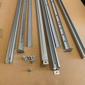 Op de afbeelding: Een set van acht zilveren metalen rails met gaten en eindkappen, en een kleine stapel schroeven.