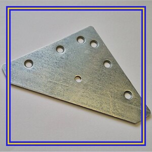 Può includere: Una piastra metallica triangolare color argento con diversi fori circolari. La piastra ha una superficie leggermente strutturata e sembra essere in acciaio zincato. I fori sono distribuiti uniformemente sulla superficie.