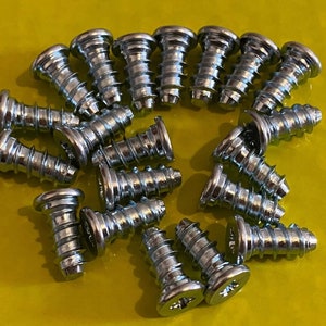 May include: A close-up of a group of silver screws with a flat head and a Phillips drive. The screws are arranged in a circle on a yellow surface.