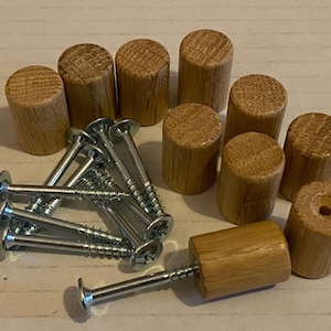 Pode incluir: Um conjunto de dez botões de madeira com acabamento natural e oito parafusos prateados. Os botões são cilíndricos e têm uma superfície lisa. Os parafusos medem aproximadamente 5 cm de comprimento.