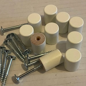 Könnte beinhalten: Ein Satz mit zehn weißen Holzgriffen mit Schrauben. Die Griffe sind rund und haben eine glatte Oberfläche. Die Schrauben sind silberfarben und haben einen Kreuzschlitz.