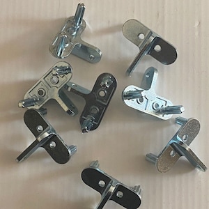 Può includere: Primo piano di otto staffe d'angolo in metallo argentato. Le staffe hanno tre fori ciascuna e sono progettate per essere utilizzate per unire due pezzi di legno ad un angolo di 90 gradi.