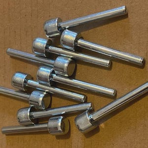 Peut inclure: Un ensemble d'épingles métalliques argentées avec des têtes arrondies et des tiges cylindriques. Les épingles sont dispersées sur une surface marron, certaines se chevauchant. Les têtes semblent texturées.