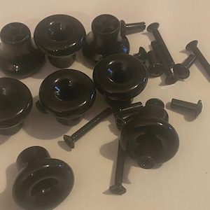 Könnte beinhalten: Eine Sammlung schwarzer Schrankknöpfe mit passenden Schrauben. Die Knöpfe haben eine abgerundete, pilzartige Form und eine glänzende Oberfläche. Verschiedene Schraubengrößen sind für die Installation enthalten.