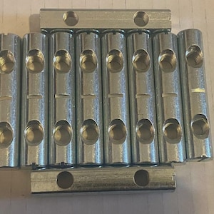 May include: A collection of silver metal connectors, each with multiple holes and threaded interiors. The cylindrical connectors have oval openings, and the rectangular bars have circular holes. The items are arranged in an organised pattern.
