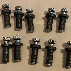 May include: Ten black and silver bolts with ribbed shafts and fluted silver tops are arranged on a light-coloured surface. The bolts are likely for furniture or other hardware applications.