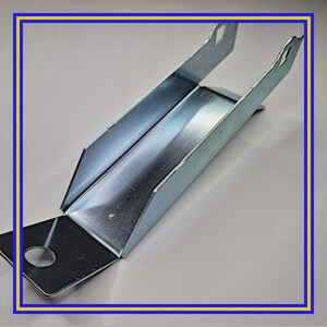 May include: A galvanized steel bracket with a rectangular base and angled sides, featuring a circular hole and two slotted tabs. The metal has a shiny, reflective surface. The bracket is designed for structural support.