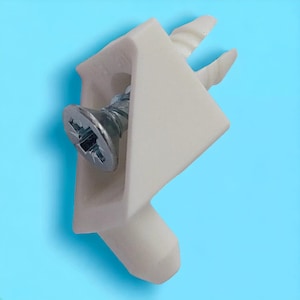 Może przedstawiać: Biały plastikowy narożnik z wkręconym śrubą przez otwór w środku. Narożnik ma dwa wystające elementy na górze i spiczasty koniec na dole.