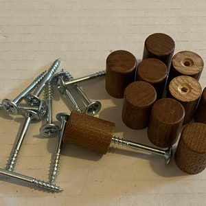 Könnte beinhalten: Ein Satz mit 10 Holzgriffen mit brauner Oberfläche und silbernen Schrauben. Die Griffe sind zylindrisch und haben eine glatte Oberfläche. Die Schrauben sind etwa 2,5 cm lang.