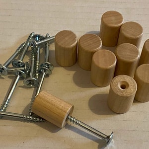 Peut inclure: Un ensemble de dix boutons en bois avec un trou au centre et dix vis argentées. Les boutons sont de couleur brun clair et ont une finition lisse.