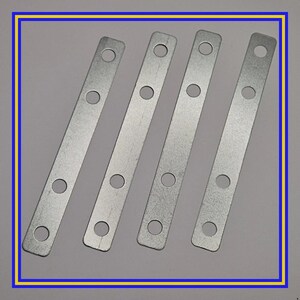 May include: Four silver metal plates with evenly spaced holes. Each plate is rectangular and has rounded corners. The plates are arranged diagonally across the frame, with a light gray background.