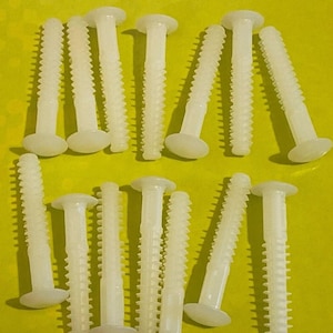 May include: A close-up of a group of white plastic screws with a flat head and a threaded shaft. The screws are arranged in two rows on a yellow surface.