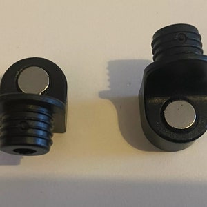 May include: Two black plastic magnetic corner brackets with a threaded end. The brackets have a silver magnet on the side.