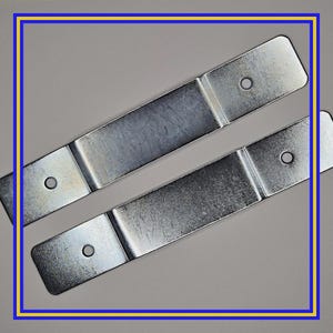 May include: Two silver-colored metal brackets with rounded ends and a single hole in each end. The brackets are rectangular with a slightly textured surface. The image is framed with a blue and yellow border.