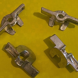 May include: Four silver metal wing nuts with a threaded center hole. The wing nuts have a flat, rectangular shape with two wings on either side. The wings are angled to allow for easy tightening and loosening.