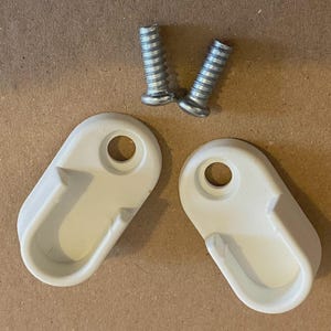 May include: Two off-white, oval-shaped closet rod holders with a curved hook design and a hole for screws. Two silver screws are also included in the image. The items are on a light brown surface.