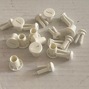 May include: A collection of white plastic hardware pieces, including screws, nuts, and washers. These pieces are commonly used for assembling furniture or other household items.