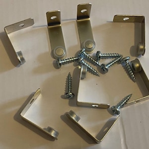 May include: A selection of metal corner brackets and screws. The brackets are L-shaped with a silver finish and small rollers. The screws are silver with a pointed end. Hardware for furniture or construction.