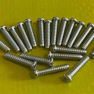 May include: A collection of shiny, silver screws with slotted heads. The screws are arranged on a bright yellow-green surface. The screws have a threaded shaft and a rounded head. The image shows a close-up view of the screws.