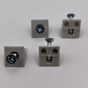 Puede incluir: Cuatro soportes de esquina de plástico blanco con agujeros para tornillos y un tornillo en cada uno. Dos de los soportes tienen un diseño de cara sonriente.