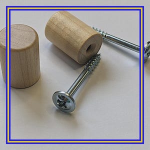 Könnte beinhalten: Nahaufnahme von Möbelknöpfen aus Holz und silbernen Schrauben. Die Knöpfe sind zylindrisch und aus hellem Holz gefertigt. Die Schrauben haben einen flachen Kopf mit kreuzförmiger Vertiefung. Beschläge für die Möbelmontage.