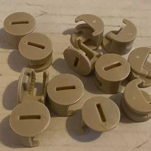 May include: A collection of beige plastic cord end caps with a slot in the center. The caps are designed to cover the ends of cords and prevent fraying.