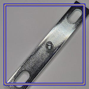May include: A silver-colored metal bracket with two oval-shaped holes and a central rivet. The bracket is rectangular and appears to be made of galvanized steel. The surface has a textured finish, reflecting light.