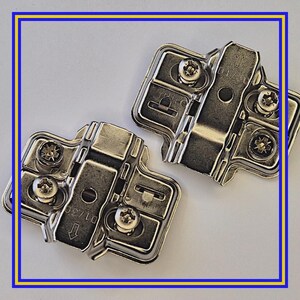 Könnte beinhalten: Zwei silberfarbene Scharniere mit Schraubenlöchern und einem Drehmechanismus. Die Scharniere sind aus Metall gefertigt und dienen zur Befestigung von Schranktüren an Rahmen. Das Bild ist mit einem blau-gelben Rahmen versehen.