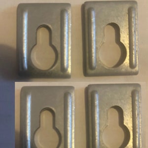 May include: Four silver metal picture hanging hooks with a keyhole design. The hooks are rectangular and have a smooth, metallic finish.