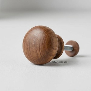 May include: A round, brown wooden cabinet knob with a visible natural wood grain pattern. The knob features a central stem and a metal screw extending from the back. The text IKEA 10122514 is printed in small black letters near the base of the knob.