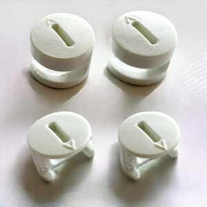 May include: Four white plastic curtain rings with a small arrow on the top. Two of the rings are taller than the other two.