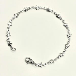 May include: A silver-toned chain bracelet featuring a series of small, evenly spaced star-shaped charms linked together. The bracelet is secured with a lobster claw clasp, creating a continuous circular design of metallic stars along the entire length.