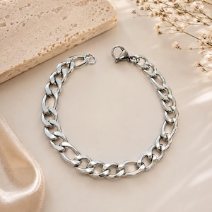 Op de afbeelding: Een zilverkleurige metalen kettingarmband met in elkaar grijpende ovale schakels en een veilige karabijnsluiting. De armband is opgebouwd uit gepolijste, reflecterende metalen segmenten die een doorlopende, uniforme lusvorm creëren.