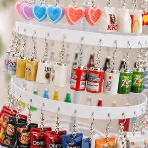 May include: A white tiered rotating display stand holding various miniature novelty earrings. The charms include heart shapes, fast food bags, beverage cans with logos like Budweiser and 7up, and snack bags featuring Lay's, Doritos, Cheetos, and Goldfish.
